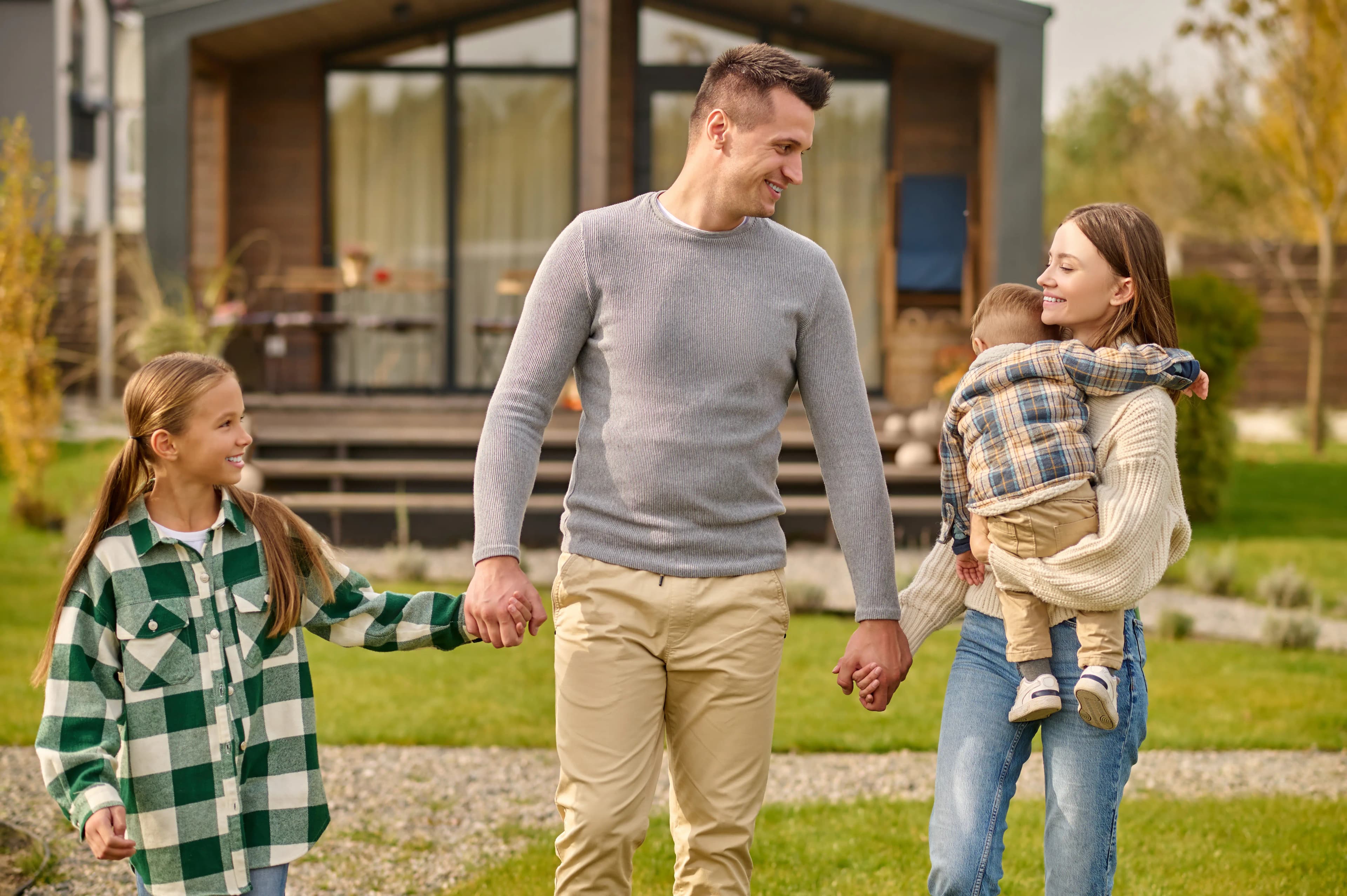 happy family holding hands walking yard outside house